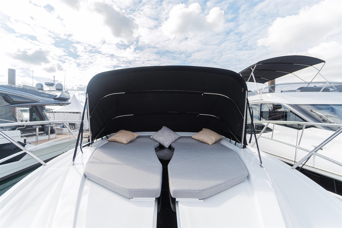 Luxury boat deck featuring two cushioned lounge areas with decorative pillows under a black canopy, surrounded by other boats.
